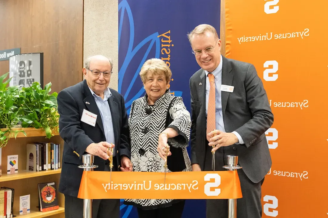 Three people cutting a ribbon during a ceremony at a library on campus.